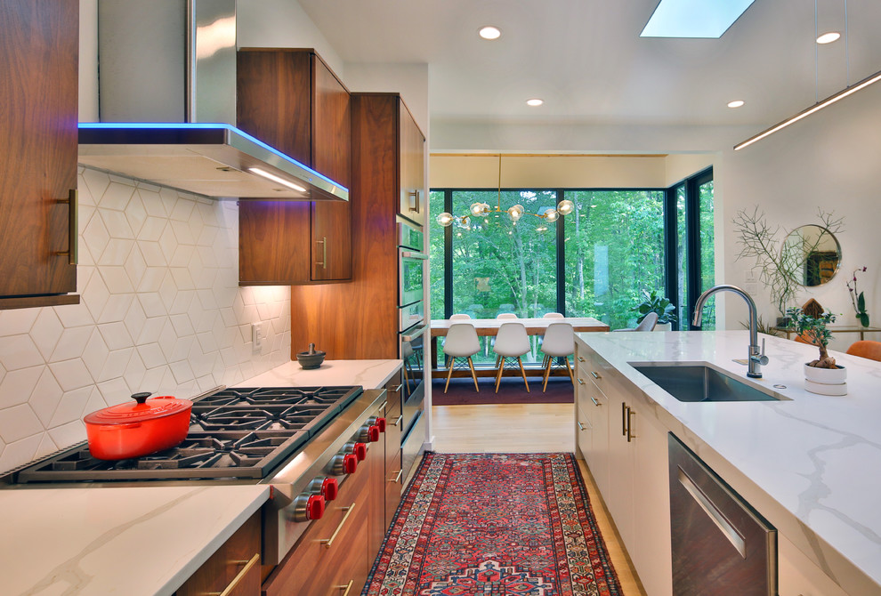 This is an example of a mid-sized modern l-shaped open plan kitchen in Raleigh with an undermount sink, flat-panel cabinets, medium wood cabinets, quartzite benchtops, white splashback, mosaic tile splashback, stainless steel appliances, light hardwood floors, with island, white floor and white benchtop.