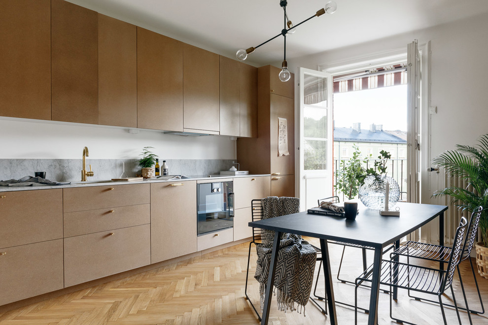 Inspiration for a mid-sized scandinavian single-wall eat-in kitchen in Stockholm with a single-bowl sink, flat-panel cabinets, beige cabinets, marble benchtops, black appliances, light hardwood floors and no island.