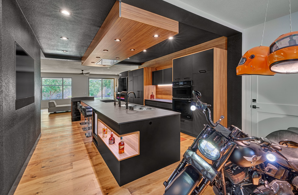 This is an example of a large modern single-wall open plan kitchen in Sacramento with an undermount sink, flat-panel cabinets, black cabinets, quartz benchtops, black appliances, medium hardwood floors, with island, brown floor and black benchtop.