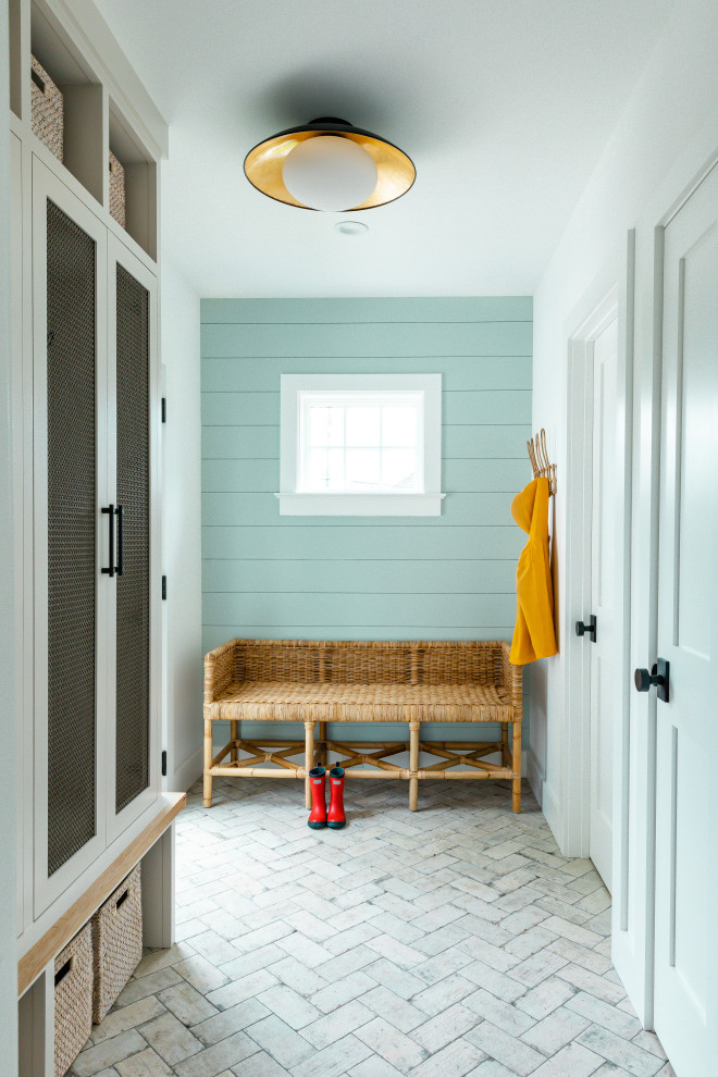 This is an example of a large beach style mudroom in Other with white walls, a single front door, a light wood front door, planked wall panelling, brick floors and beige floor.