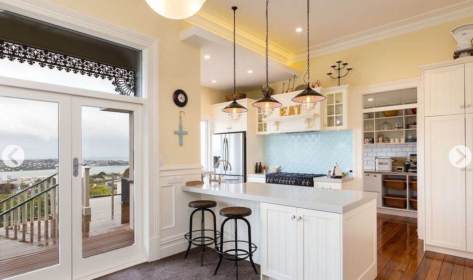 Large transitional galley eat-in kitchen in Dunedin with a farmhouse sink, shaker cabinets, white cabinets, granite benchtops, blue splashback, metal splashback, stainless steel appliances, with island and white benchtop.