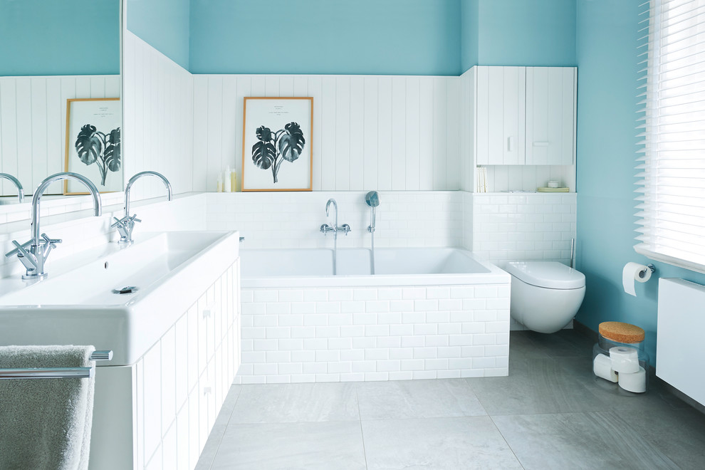 This is an example of a mid-sized country bathroom in Hamburg with white cabinets, a drop-in tub, a wall-mount toilet, subway tile, blue walls, a vessel sink and brown floor.