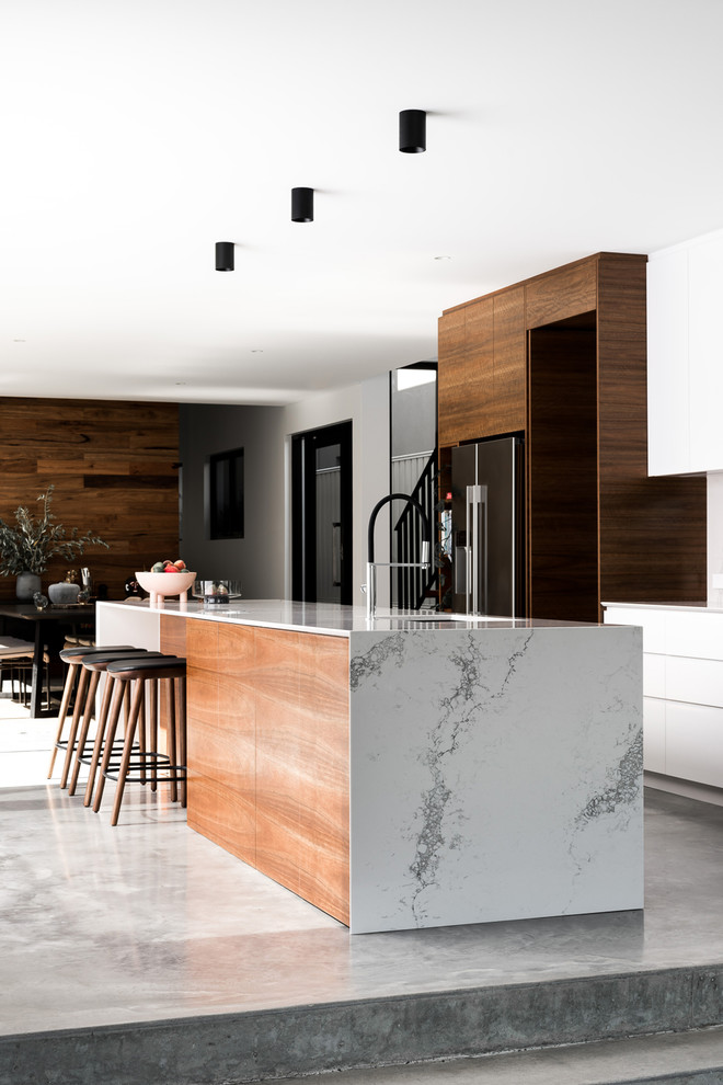 Inspiration for a large contemporary galley open plan kitchen in Perth with an undermount sink, flat-panel cabinets, white cabinets, quartz benchtops, white splashback, stone slab splashback, black appliances, concrete floors, with island and grey floor.