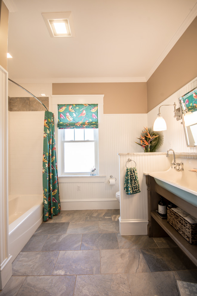 This is an example of a large traditional kids bathroom in Providence with furniture-like cabinets, distressed cabinets, marble benchtops, gray tile, porcelain tile, an alcove tub, a shower/bathtub combo, a two-piece toilet, a trough sink, beige walls and porcelain floors.
