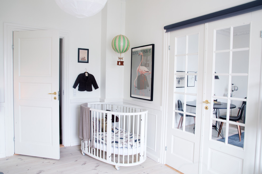This is an example of a mid-sized scandinavian gender-neutral nursery in Copenhagen with white walls, light hardwood floors and white floor.