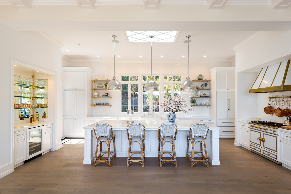 Photo of a large transitional u-shaped kitchen in San Francisco with a farmhouse sink, recessed-panel cabinets, white cabinets, marble benchtops, white splashback, subway tile splashback, medium hardwood floors, with island, white benchtop, coloured appliances and brown floor.