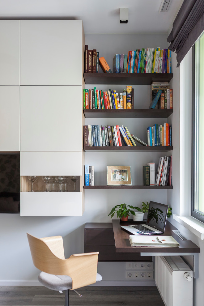 Photo of a small contemporary home office in Moscow with a library, white walls, a built-in desk and brown floor.