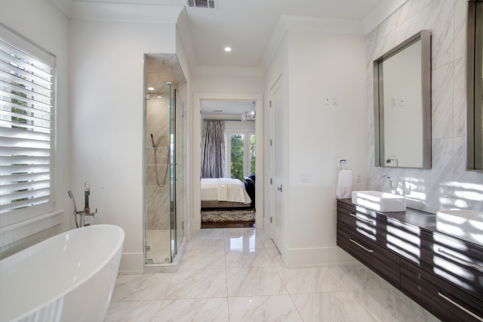 Photo of a large transitional master bathroom in New Orleans with flat-panel cabinets, dark wood cabinets, a freestanding tub, a corner shower, a two-piece toilet, white tile, white walls, marble floors, a vessel sink, wood benchtops, white floor, a hinged shower door, white benchtops, an enclosed toilet, a single vanity, a floating vanity and vaulted.