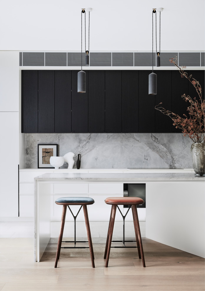 This is an example of a large contemporary l-shaped open plan kitchen in Sydney with a double-bowl sink, flat-panel cabinets, white cabinets, marble benchtops, grey splashback, marble splashback, black appliances, medium hardwood floors, with island, brown floor and grey benchtop.