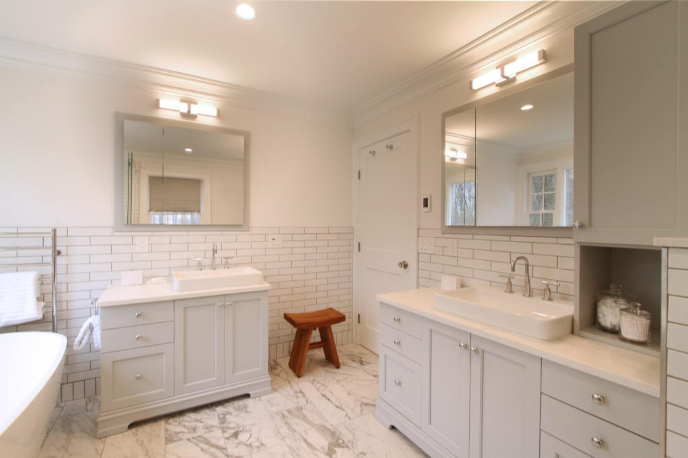 Inspiration for a mid-sized transitional master bathroom in New York with shaker cabinets, white cabinets, a freestanding tub, a corner shower, a bidet, white tile, ceramic tile, white walls, porcelain floors, a vessel sink, engineered quartz benchtops, grey floor, a sliding shower screen, beige benchtops, a double vanity and a freestanding vanity.