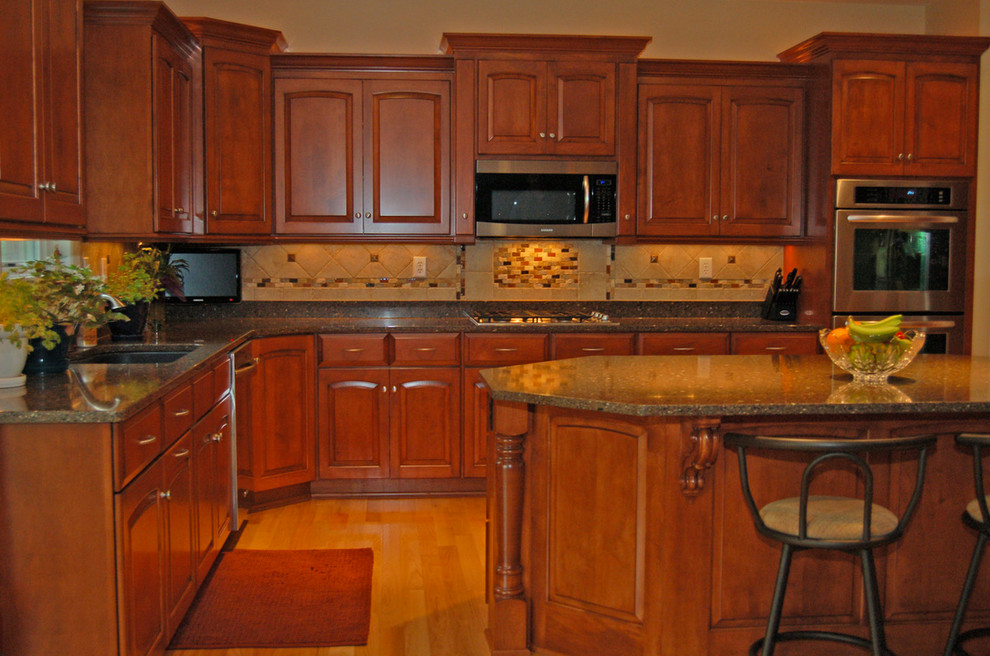 Inspiration for a mid-sized transitional u-shaped light wood floor eat-in kitchen remodel with an undermount sink, raised-panel cabinets, medium tone wood cabinets, granite countertops, beige backsplash, cement tile backsplash, stainless steel appliances and an island