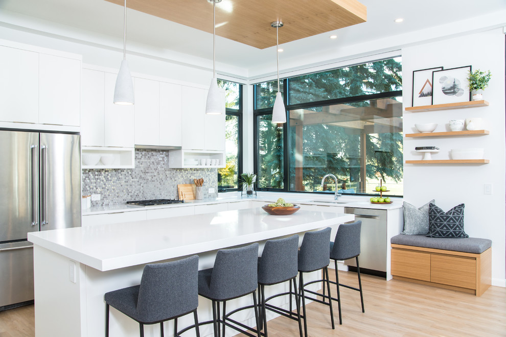 Inspiration for a mid-sized contemporary l-shaped open plan kitchen in Edmonton with an undermount sink, flat-panel cabinets, white cabinets, quartz benchtops, metallic splashback, mosaic tile splashback, stainless steel appliances, light hardwood floors, with island, white benchtop and beige floor.