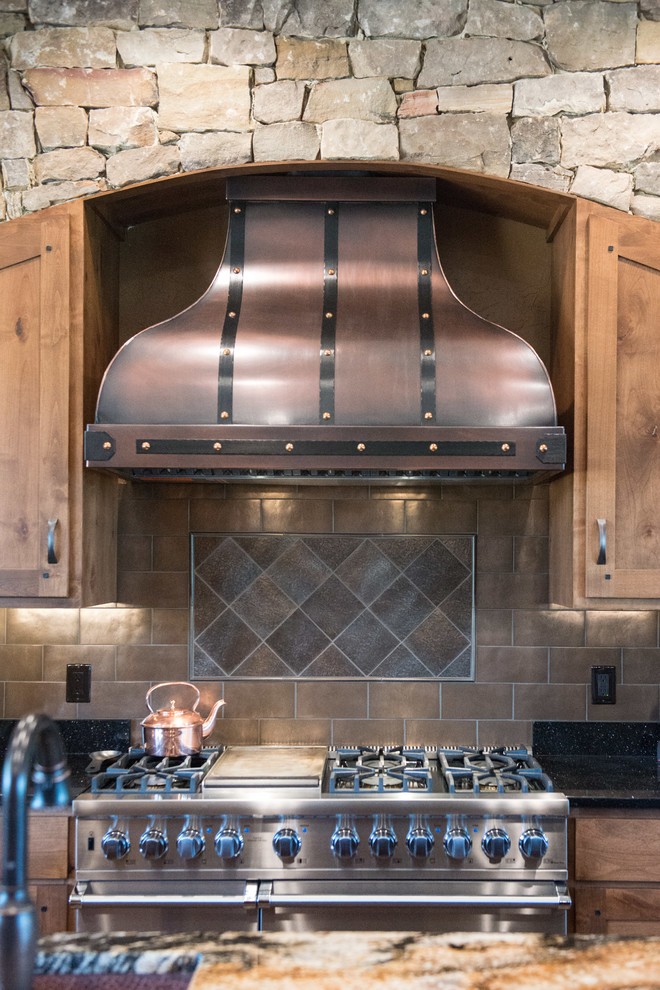 Huge mountain style u-shaped medium tone wood floor home design photo with a double-bowl sink, shaker cabinets, medium tone wood cabinets, granite countertops, metallic backsplash, stainless steel appliances and two islands