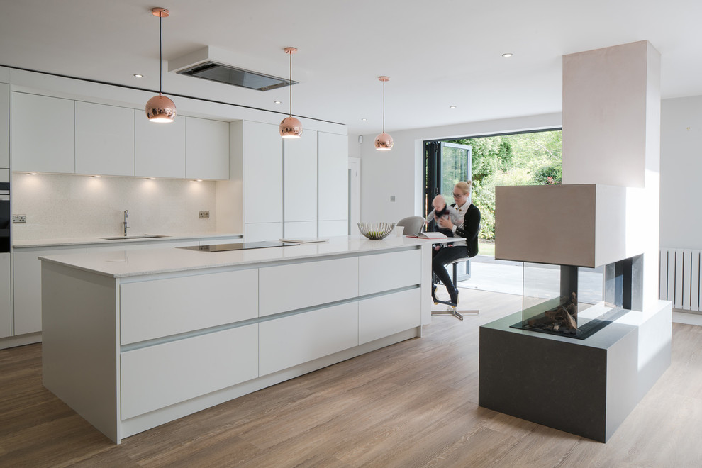 Modern kitchen in West Midlands with an undermount sink, flat-panel cabinets, white cabinets, white splashback, light hardwood floors, with island, beige floor and white benchtop.