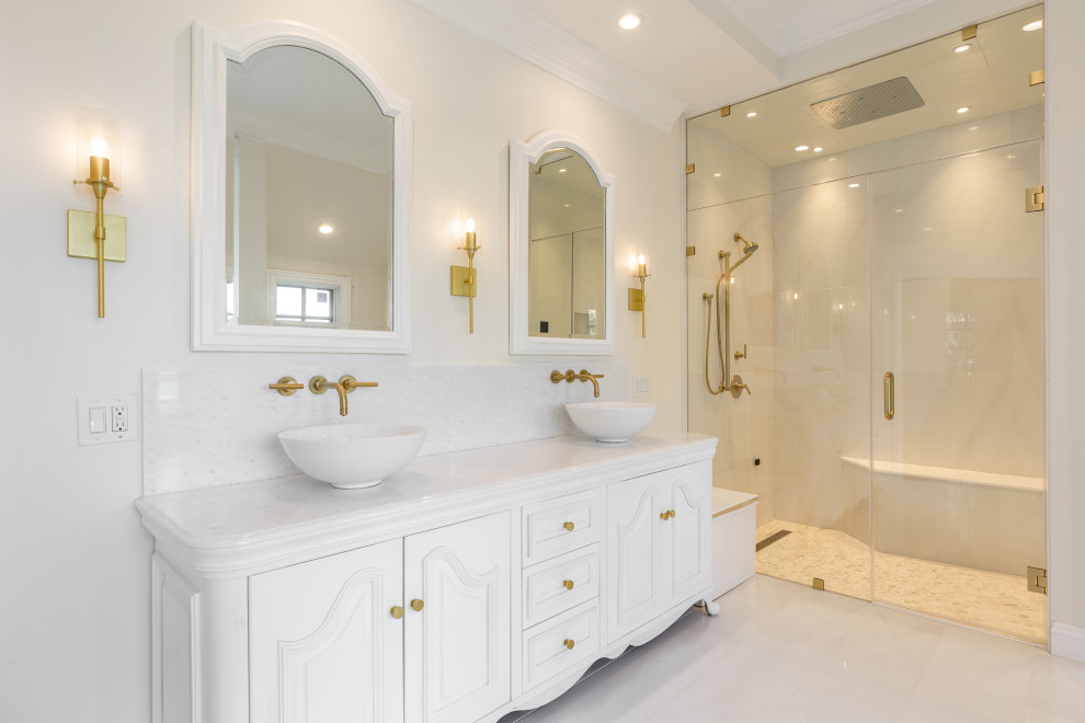 Стильный дизайн: большая главная ванная комната в классическом стиле с белыми фасадами, накладной ванной, душем без бортиков, биде, белой плиткой, мраморной плиткой, белыми стенами, мраморным полом, подвесной раковиной, мраморной столешницей, белым полом, душем с распашными дверями, белой столешницей, сиденьем для душа, тумбой под две раковины, напольной тумбой и фасадами с утопленной филенкой - последний тренд