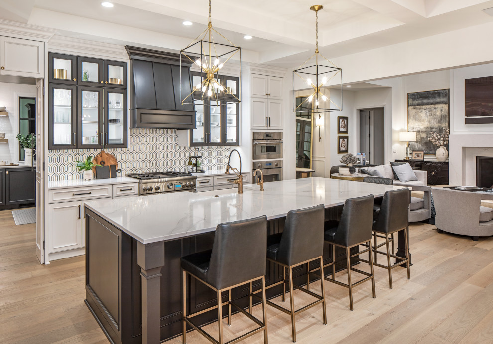 Expansive transitional l-shaped eat-in kitchen in Omaha with a farmhouse sink, recessed-panel cabinets, black cabinets, quartz benchtops, panelled appliances, light hardwood floors, with island, white benchtop and exposed beam.