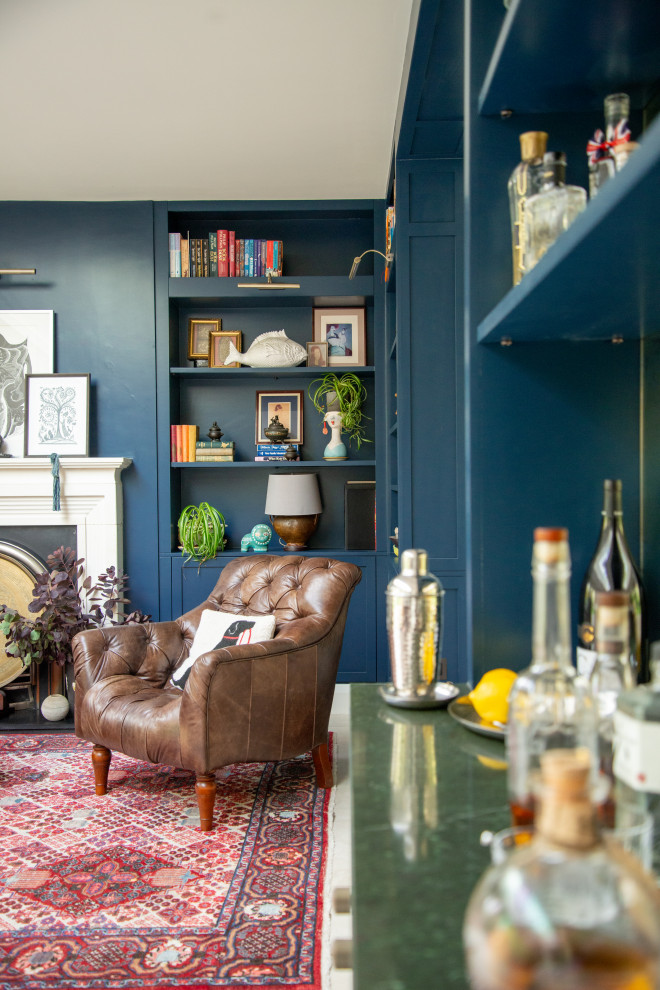 This is an example of a large eclectic open concept living room in Hertfordshire with a home bar, blue walls, porcelain floors, a standard fireplace, a plaster fireplace surround, no tv and beige floor.