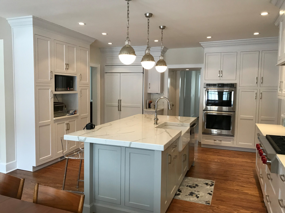 Large transitional u-shaped medium tone wood floor and brown floor eat-in kitchen photo with a farmhouse sink, recessed-panel cabinets, white cabinets, quartz countertops, white backsplash, subway tile backsplash, stainless steel appliances, an island and white countertops