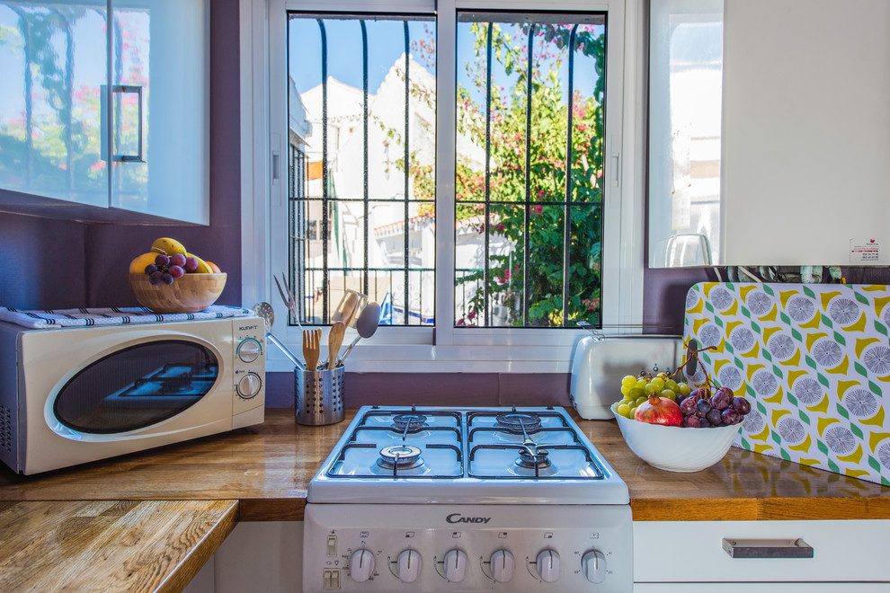 Photo of a small mediterranean separate kitchen in Other with a double-bowl sink, flat-panel cabinets, white cabinets, wood benchtops, white splashback, timber splashback, white appliances, medium hardwood floors and brown floor.