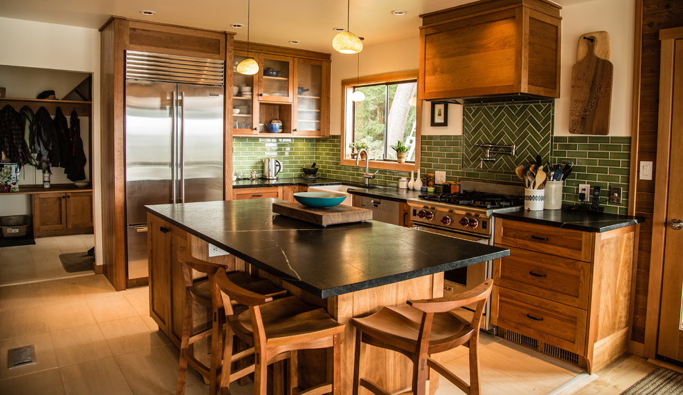 Photo of a small country l-shaped eat-in kitchen in Vancouver with a farmhouse sink, shaker cabinets, medium wood cabinets, soapstone benchtops, green splashback, subway tile splashback, stainless steel appliances, porcelain floors, with island and beige floor.
