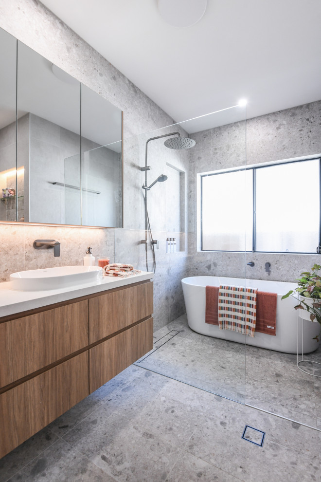 This is an example of a medium sized contemporary family bathroom in Sydney with light wood cabinets, a freestanding bath, a walk-in shower, grey tiles, multi-coloured tiles, ceramic flooring, a vessel sink, engineered stone worktops, grey floors, an open shower, white worktops, a wall niche, a single sink and a floating vanity unit.