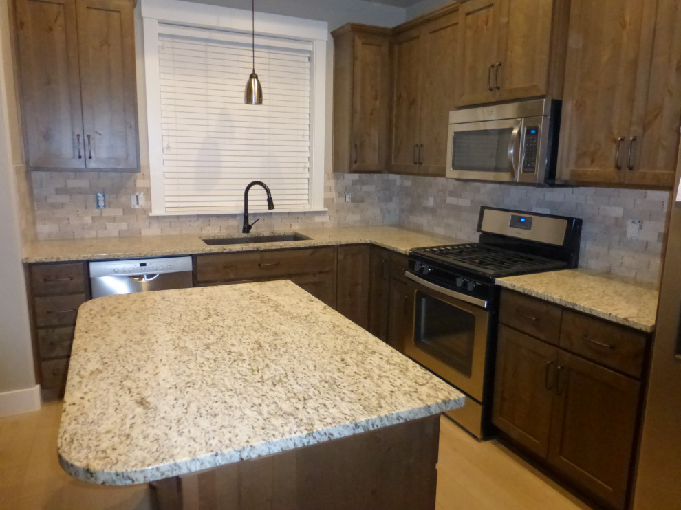 Mid-sized l-shaped eat-in kitchen photo in Boise with an undermount sink, medium tone wood cabinets, granite countertops, multicolored backsplash, limestone backsplash, stainless steel appliances, an island and multicolored countertops
