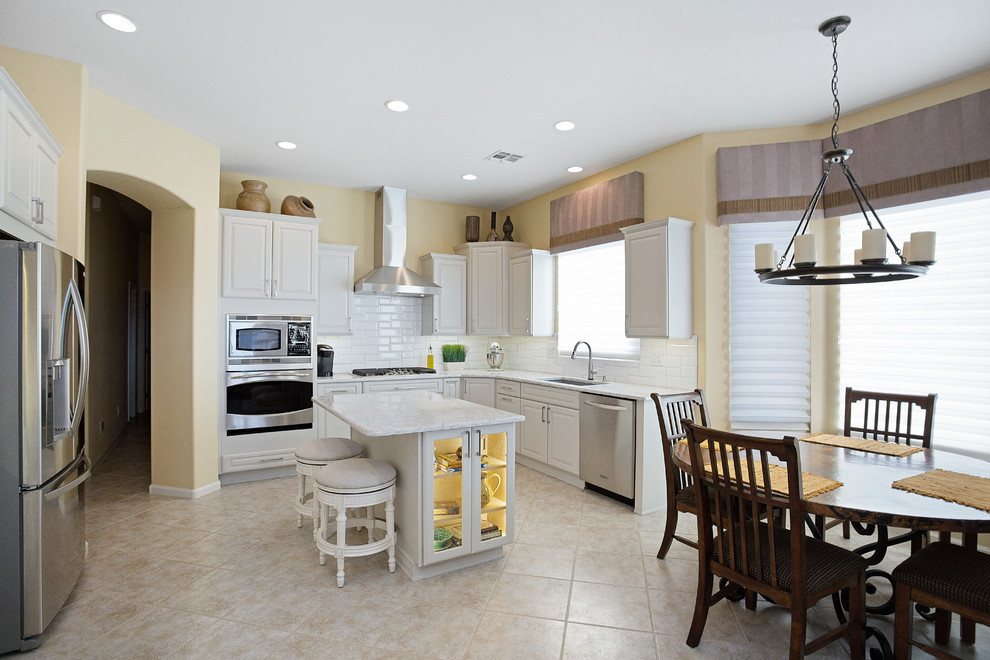 Inspiration for a mid-sized transitional single-wall ceramic tile and beige floor eat-in kitchen remodel with an undermount sink, raised-panel cabinets, white cabinets, quartz countertops, white backsplash, porcelain backsplash, stainless steel appliances and an island