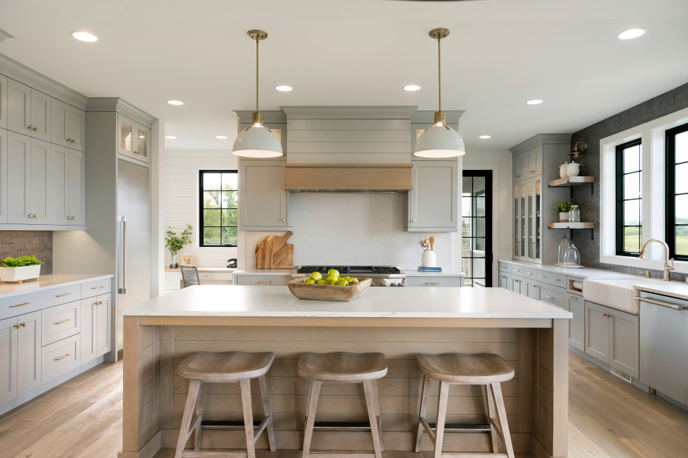 Inspiration for a transitional u-shaped kitchen in Minneapolis with a farmhouse sink, shaker cabinets, grey cabinets, grey splashback, stainless steel appliances, with island, white benchtop, medium hardwood floors and brown floor.