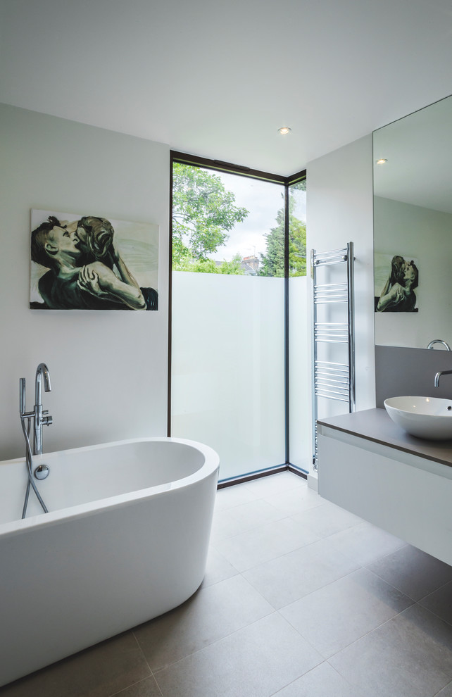 This is an example of a mid-sized contemporary kids bathroom in London with flat-panel cabinets, white cabinets, a freestanding tub, white tile, white walls, terrazzo floors, quartzite benchtops, grey floor and brown benchtops.