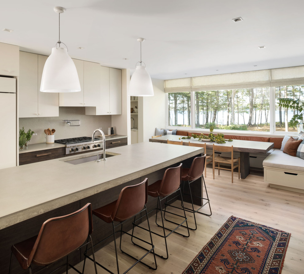 Photo of a large contemporary galley kitchen/diner in Portland Maine with a submerged sink, flat-panel cabinets, concrete worktops, grey splashback, ceramic splashback, integrated appliances, light hardwood flooring, an island, grey worktops and brown floors.