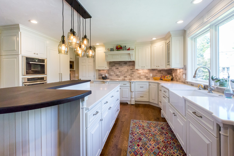 Eat-in kitchen - mid-sized transitional u-shaped medium tone wood floor eat-in kitchen idea in Boston with a farmhouse sink, raised-panel cabinets, white cabinets, quartz countertops, gray backsplash, stone tile backsplash, paneled appliances and an island