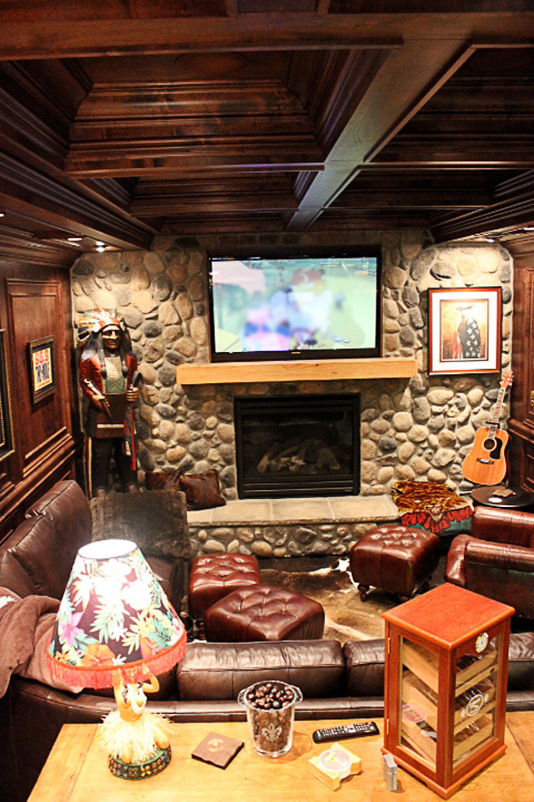 Mid-sized mountain style walk-out dark wood floor and brown floor basement photo with brown walls, a standard fireplace and a stone fireplace