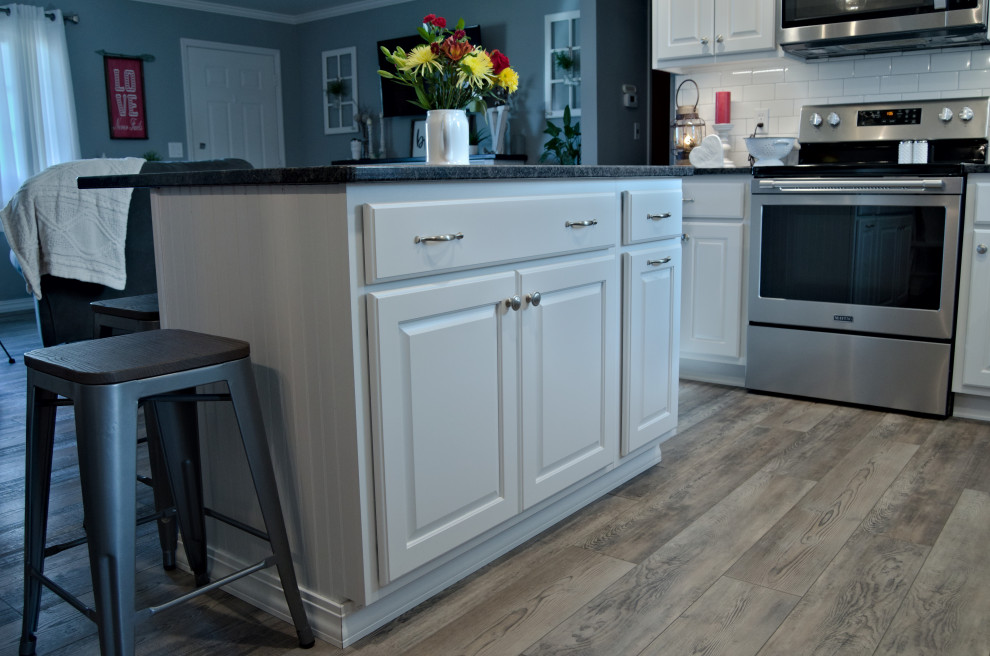 Inspiration for a l-shaped kitchen remodel with raised-panel cabinets, white cabinets, granite countertops, white backsplash, stainless steel appliances, an island and black countertops