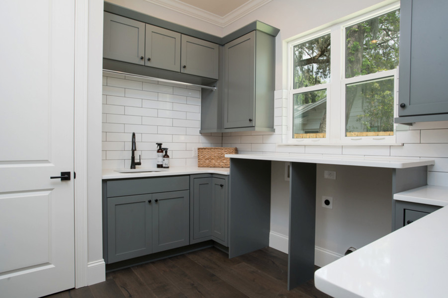 Design ideas for a mid-sized traditional u-shaped utility room in Orlando with an undermount sink, shaker cabinets, grey cabinets, quartz benchtops, white walls, porcelain floors, a side-by-side washer and dryer, brown floor and white benchtop.