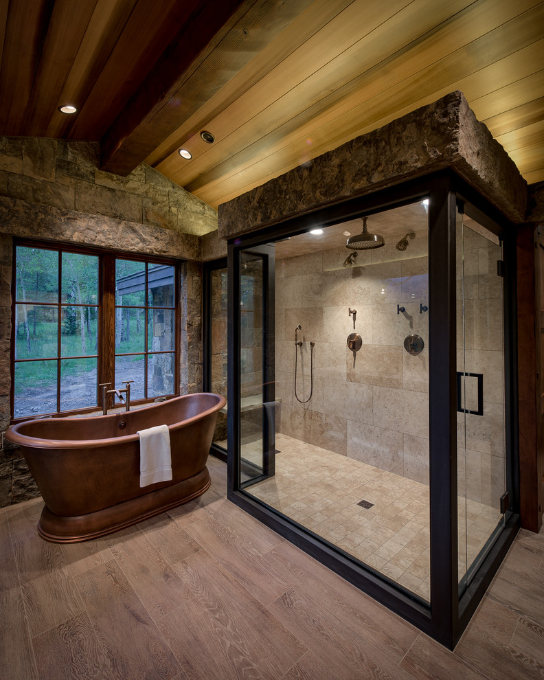 Design ideas for a country master bathroom in Denver with a freestanding tub, a double shower, brown tile, stone slab, beige walls, light hardwood floors, wood benchtops, beige floor and a hinged shower door.