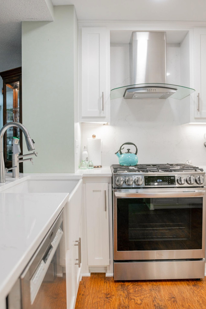 Photo of a small traditional u-shaped enclosed kitchen in Minneapolis with a belfast sink, shaker cabinets, white cabinets, engineered stone countertops, white splashback, engineered quartz splashback, stainless steel appliances, vinyl flooring, no island, brown floors and white worktops.