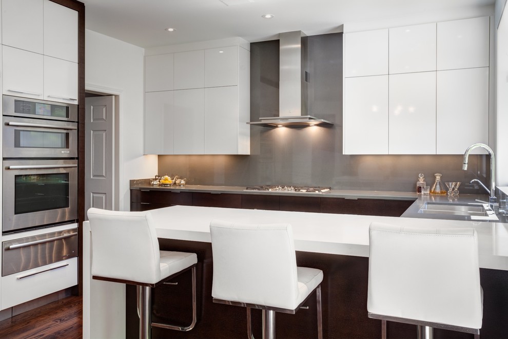 Photo of a large contemporary u-shaped eat-in kitchen in Toronto with flat-panel cabinets, white cabinets, quartz benchtops, grey splashback, stone slab splashback, stainless steel appliances, dark hardwood floors, a peninsula and a double-bowl sink.