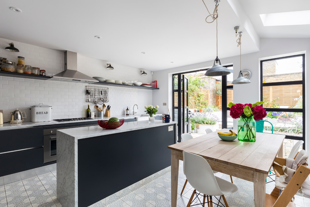 Photo of a contemporary galley eat-in kitchen in London with a farmhouse sink, flat-panel cabinets, blue cabinets, white splashback, subway tile splashback, stainless steel appliances and with island.