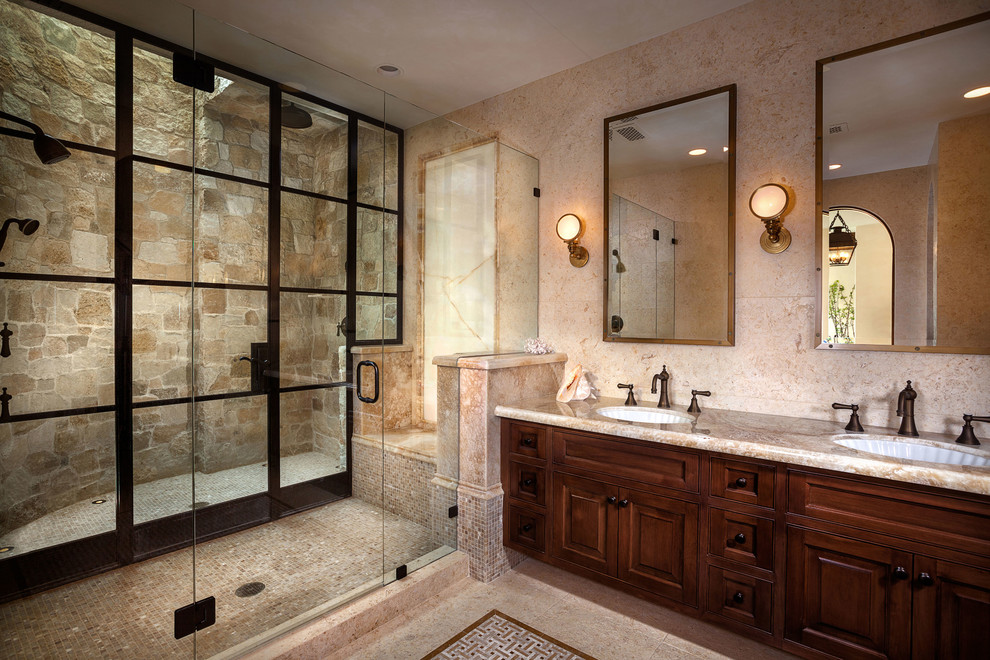 Large mediterranean master bathroom in Orange County with raised-panel cabinets, dark wood cabinets, an alcove shower, beige tile, stone tile, beige walls, an undermount sink, limestone benchtops, beige floor and a hinged shower door.