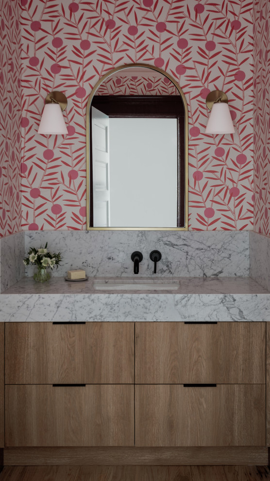 Стильный дизайн: ванная комната в стиле фьюжн с плоскими фасадами, светлыми деревянными фасадами, розовыми стенами, паркетным полом среднего тона, врезной раковиной, мраморной столешницей, коричневым полом, белой столешницей, тумбой под одну раковину, встроенной тумбой и обоями на стенах - последний тренд