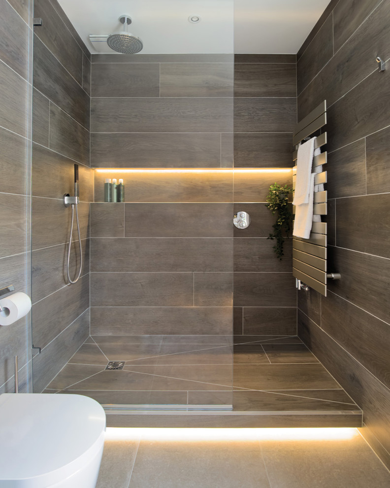 Ispirazione per una grande stanza da bagno padronale minimal con ante di vetro, ante grigie, doccia aperta, WC sospeso, piastrelle marroni, piastrelle in gres porcellanato, pavimento in gres porcellanato, lavabo sospeso, top in vetro, doccia aperta, un lavabo e mobile bagno sospeso