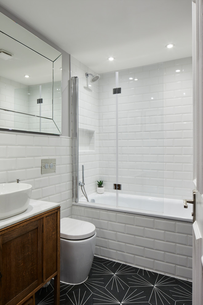 Photo of a mid-sized contemporary 3/4 bathroom in London with medium wood cabinets, an alcove tub, a shower/bathtub combo, a wall-mount toilet, white tile, porcelain tile, grey walls, a vessel sink, black floor, white benchtops, a niche, a single vanity, a freestanding vanity and flat-panel cabinets.