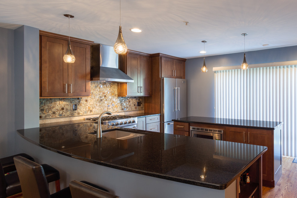 Mid-sized transitional l-shaped eat-in kitchen in Chicago with a double-bowl sink, shaker cabinets, medium wood cabinets, multi-coloured splashback, mosaic tile splashback, stainless steel appliances, medium hardwood floors, with island, granite benchtops, blue floor and brown benchtop.