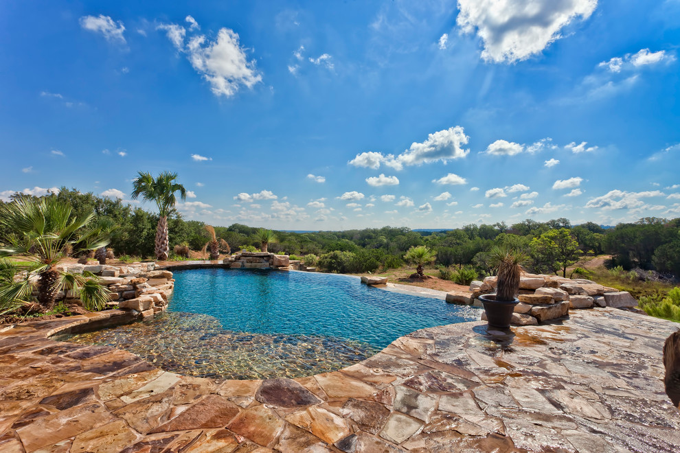 Photo of an expansive traditional backyard custom-shaped infinity pool in Austin with a water feature and natural stone pavers.