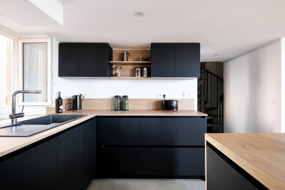 Inspiration for a large industrial open plan kitchen in Lyon with with island, an undermount sink, flat-panel cabinets, black cabinets, laminate benchtops, beige splashback, timber splashback, panelled appliances, concrete floors, grey floor, beige benchtop and exposed beam.