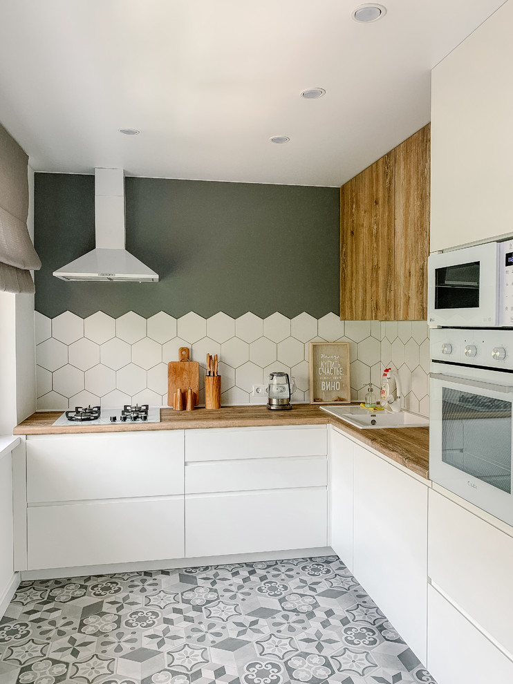 This is an example of a contemporary kitchen in Other with a drop-in sink, flat-panel cabinets, white cabinets, white splashback, grey floor and brown benchtop.