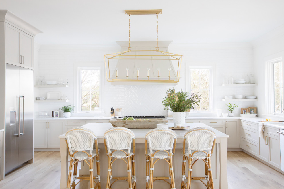 Inspiration for a beach style u-shaped kitchen in Charleston with an undermount sink, shaker cabinets, beige cabinets, white splashback, light hardwood floors, with island, beige floor and white benchtop.