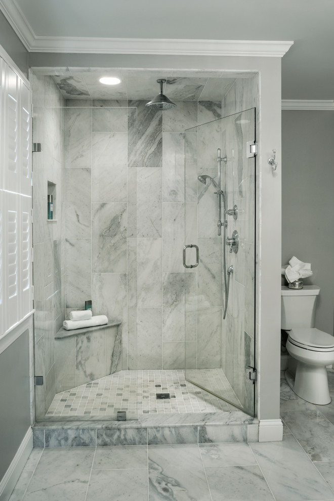 This is an example of a large transitional master bathroom in Providence with a corner shower, a two-piece toilet, gray tile, marble, grey walls, marble floors, grey floor, a hinged shower door and a shower seat.