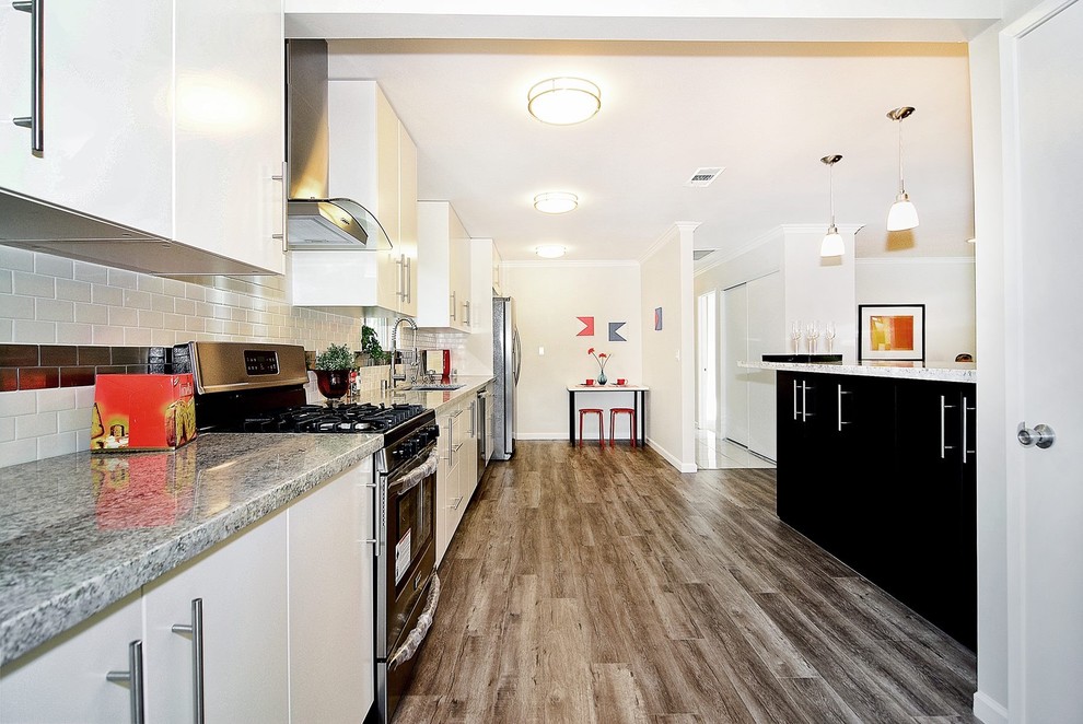 Example of a large transitional single-wall medium tone wood floor open concept kitchen design with a single-bowl sink, flat-panel cabinets, white cabinets, multicolored backsplash, stainless steel appliances and an island
