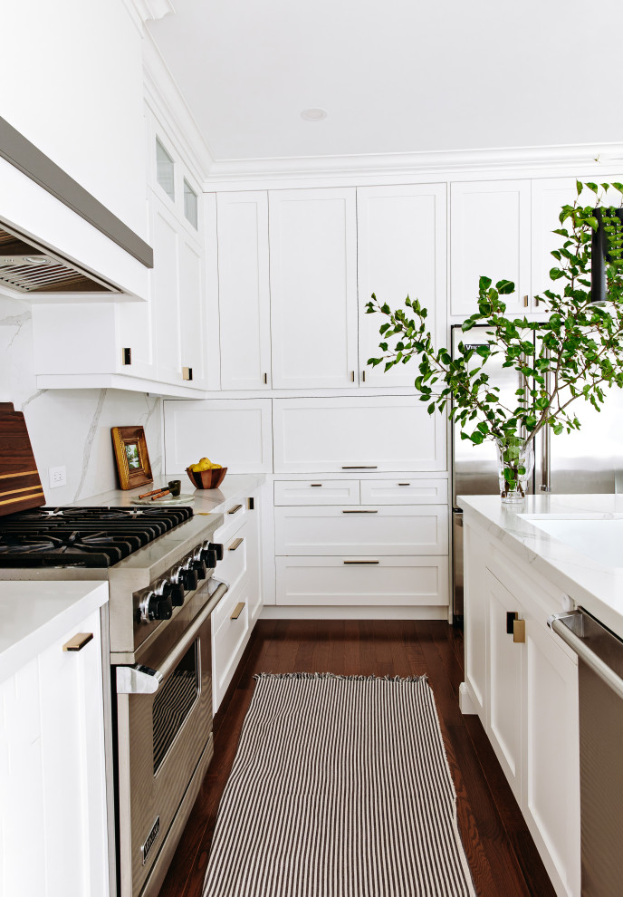 Eat-in kitchen - mid-sized transitional l-shaped dark wood floor and brown floor eat-in kitchen idea in Toronto with an undermount sink, shaker cabinets, white cabinets, quartz countertops, white backsplash, quartz backsplash, black appliances, an island and white countertops